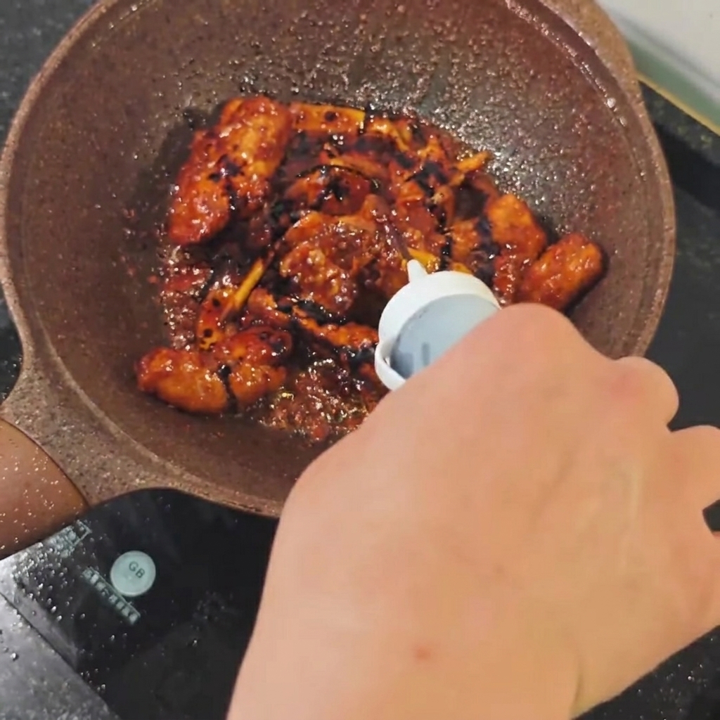 Sauce soja foncée versée depuis une petite bouteille dans une poêle de travers de porc qui dorent.