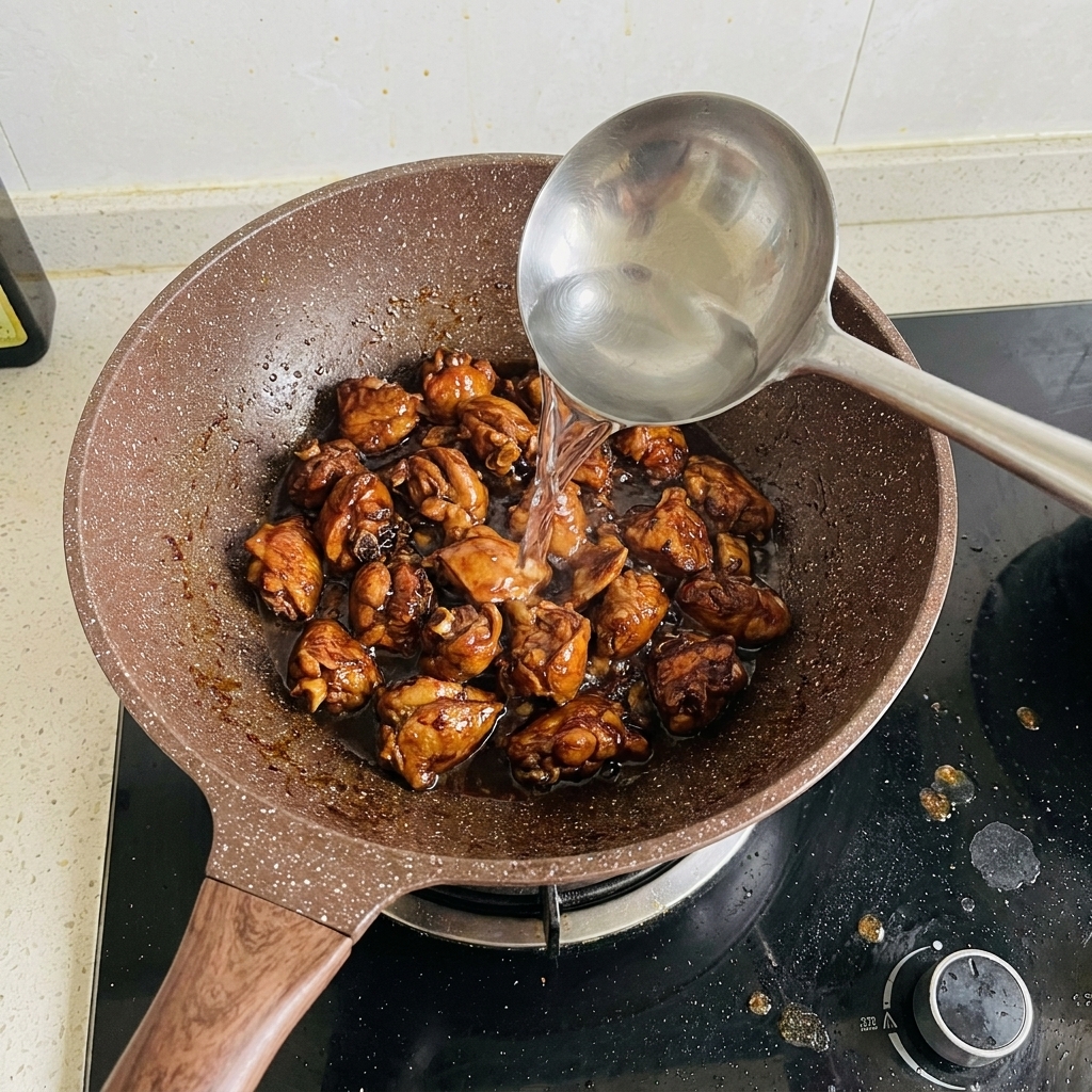 Eau versée à la louche dans une poêle remplie de travers de porc dorés.