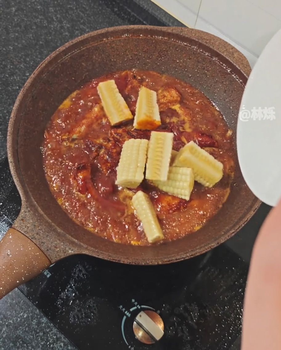 Morceaux de maïs frais ajoutés dans une poêle de travers de porc mijotant dans une sauce épicée.