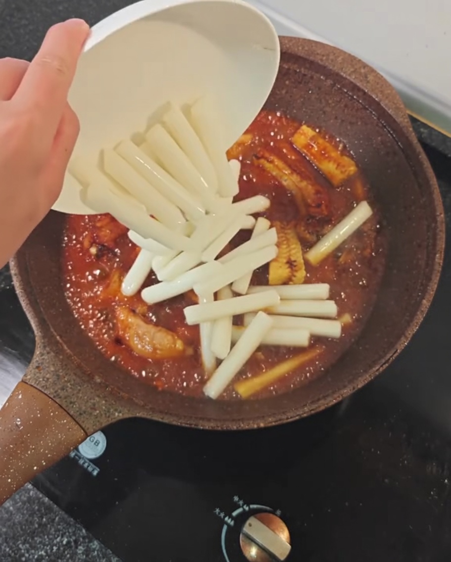 Gâteaux de riz jetés dans une poêle contenant les travers de porc, le maïs et la sauce de braisage épicée.