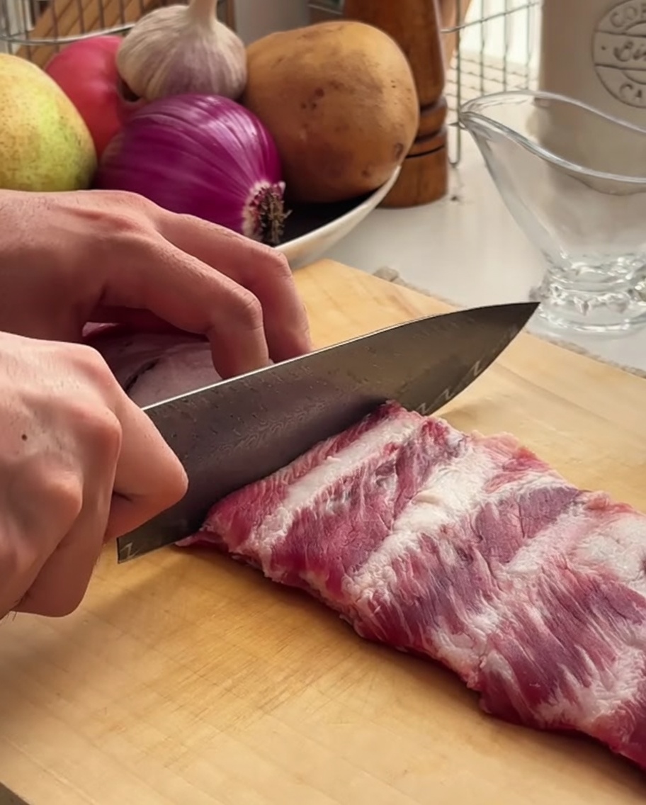 Un chef utilise un couteau bien aiguisé pour couper un travers de porc sur une planche en bois.