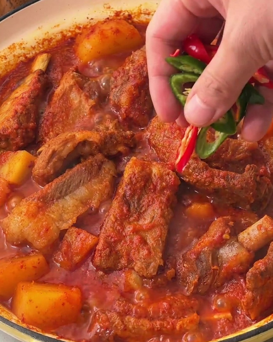 Une main saupoudre des tranches de piment frais vert et rouge sur la surface du ragoût de porc coréen.