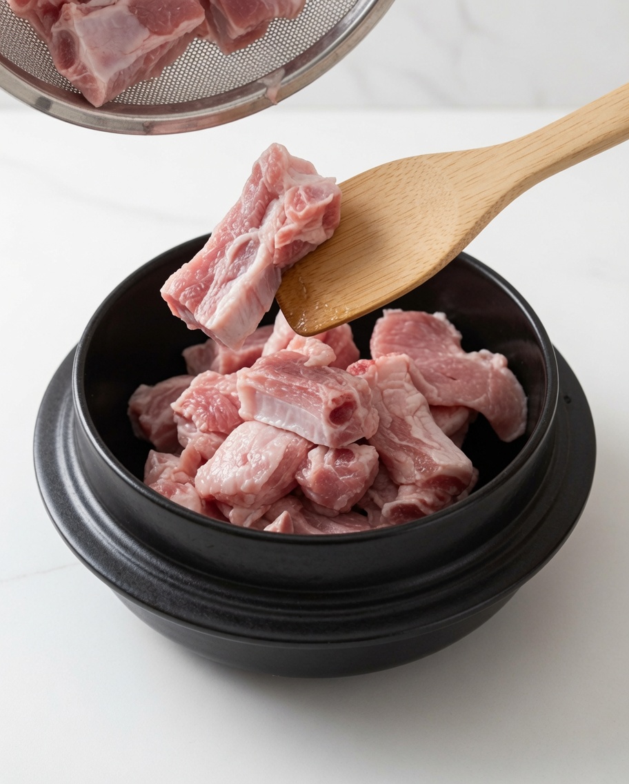Travers de porc sautés dans une marmite avec de lhuile et du sucre blanc à laide dune cuillère en bois.