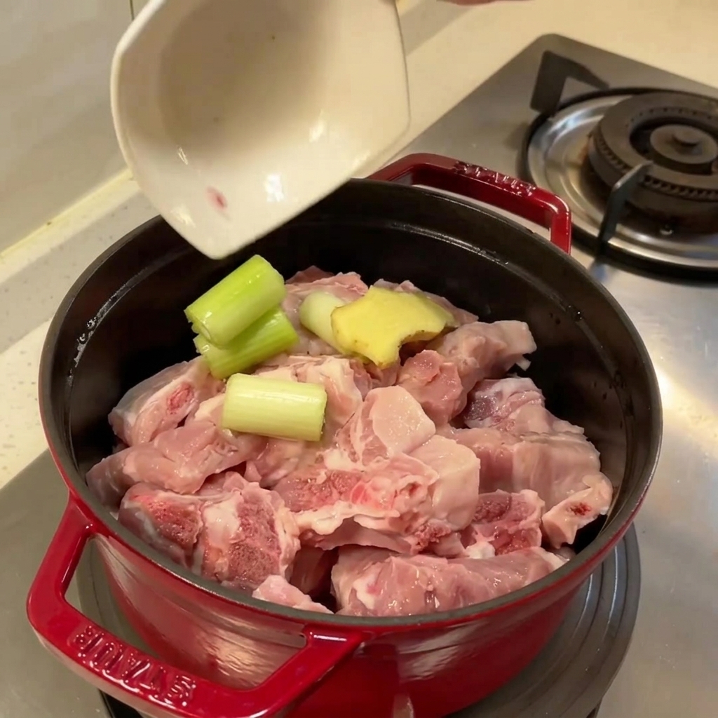 Casserole remplie de travers de porc crus, de gingembre et doignon vert prêts à bouillir.