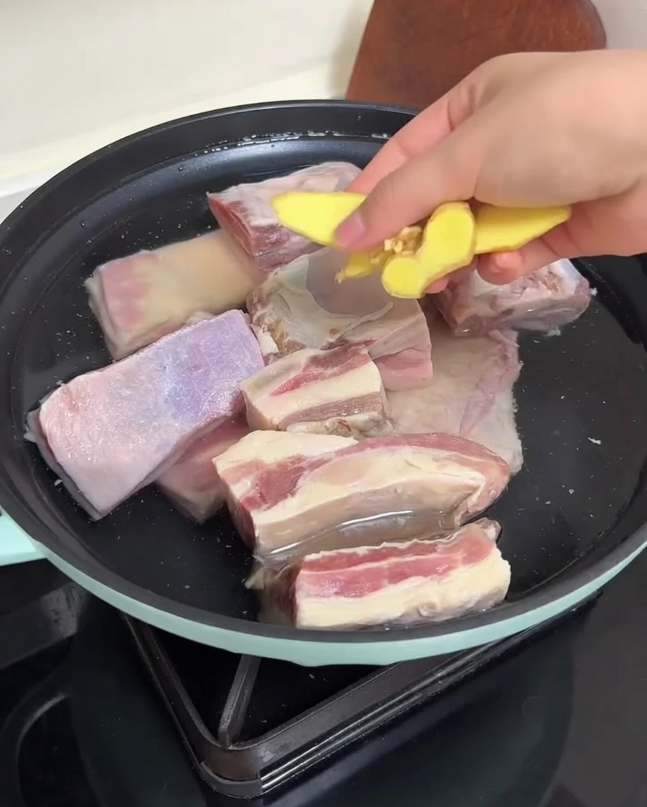 Côtes de bœuf dans une casserole avec de leau et des tranches de gingembre en préparation pour le blanchiment.