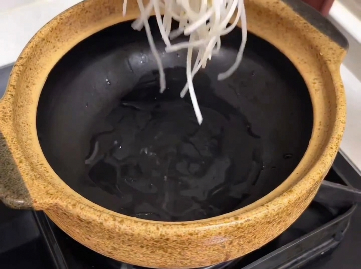 Un pot de service en céramique préparé avec des nouilles de verre, des côtes de bœuf tendres et des morceaux de radis placés à lintérieur.
