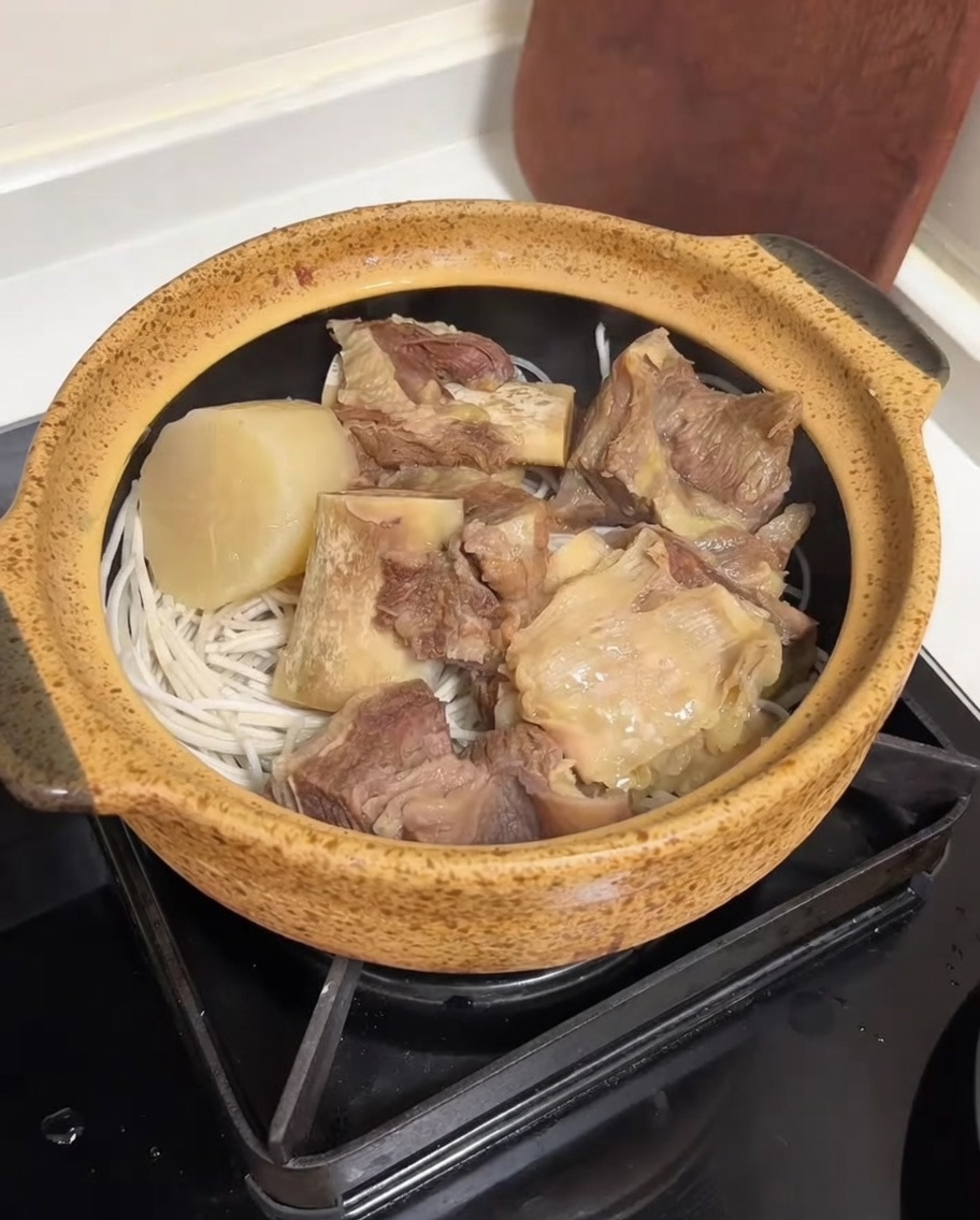 Un bouillon dos de bœuf clair et riche versé dun cuiseur de riz dans un pot en céramique rempli de côtes de bœuf, de radis et de nouilles.