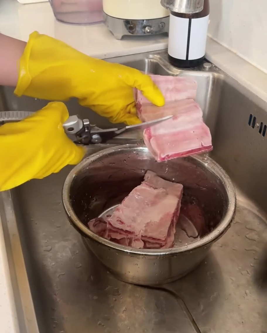 Mains portant des gants jaunes utilisant des ciseaux de cuisine pour couper les ribs.