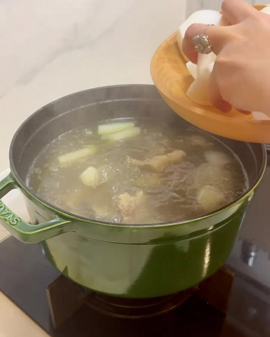 Main ajoutant de gros morceaux de radis coréen blanc dans la marmite de bouillon.