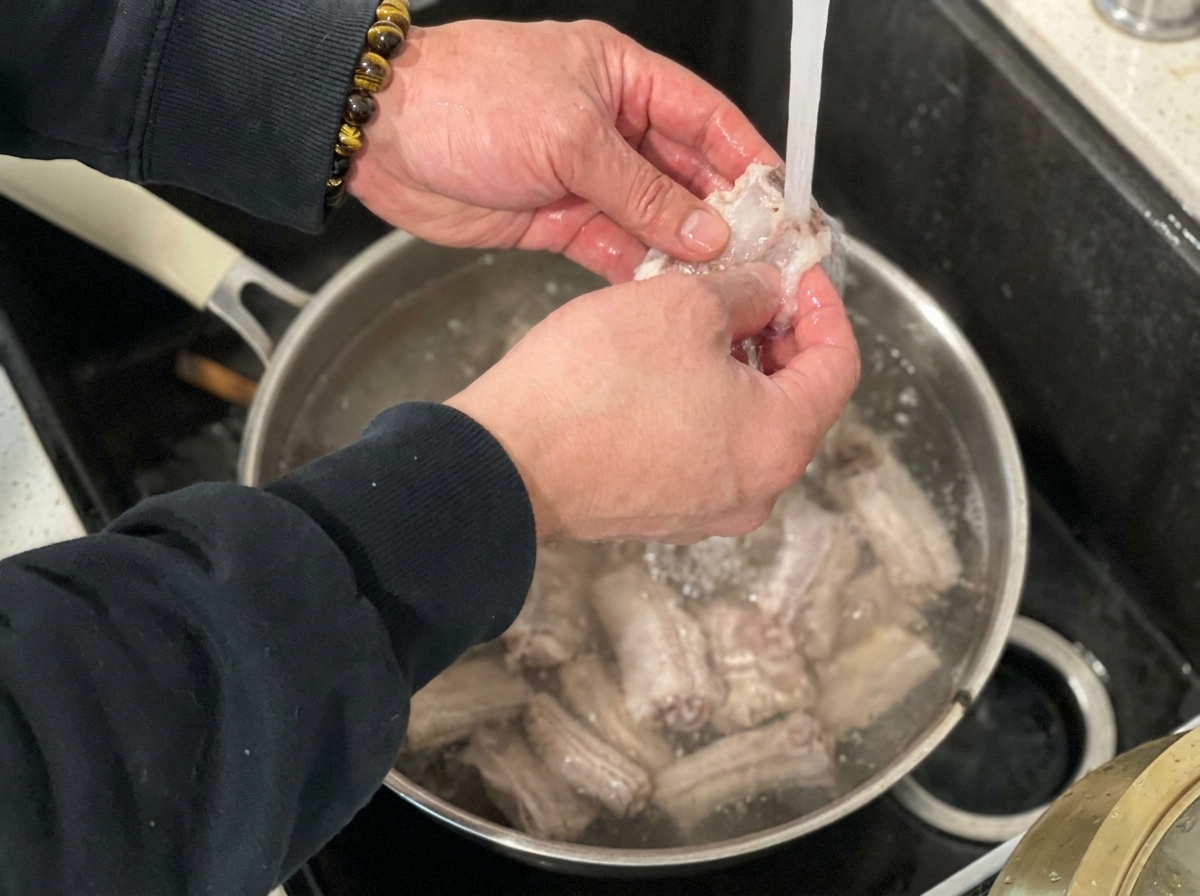 Côtes de porc blanchies en train dêtre rincées sous leau courante du robinet de la cuisine.