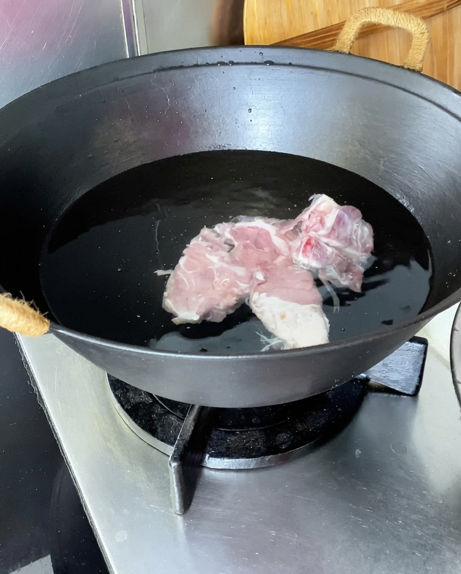 Échine de porc dans un wok deau froide avec du gingembre, des cébettes et du vin de cuisine.