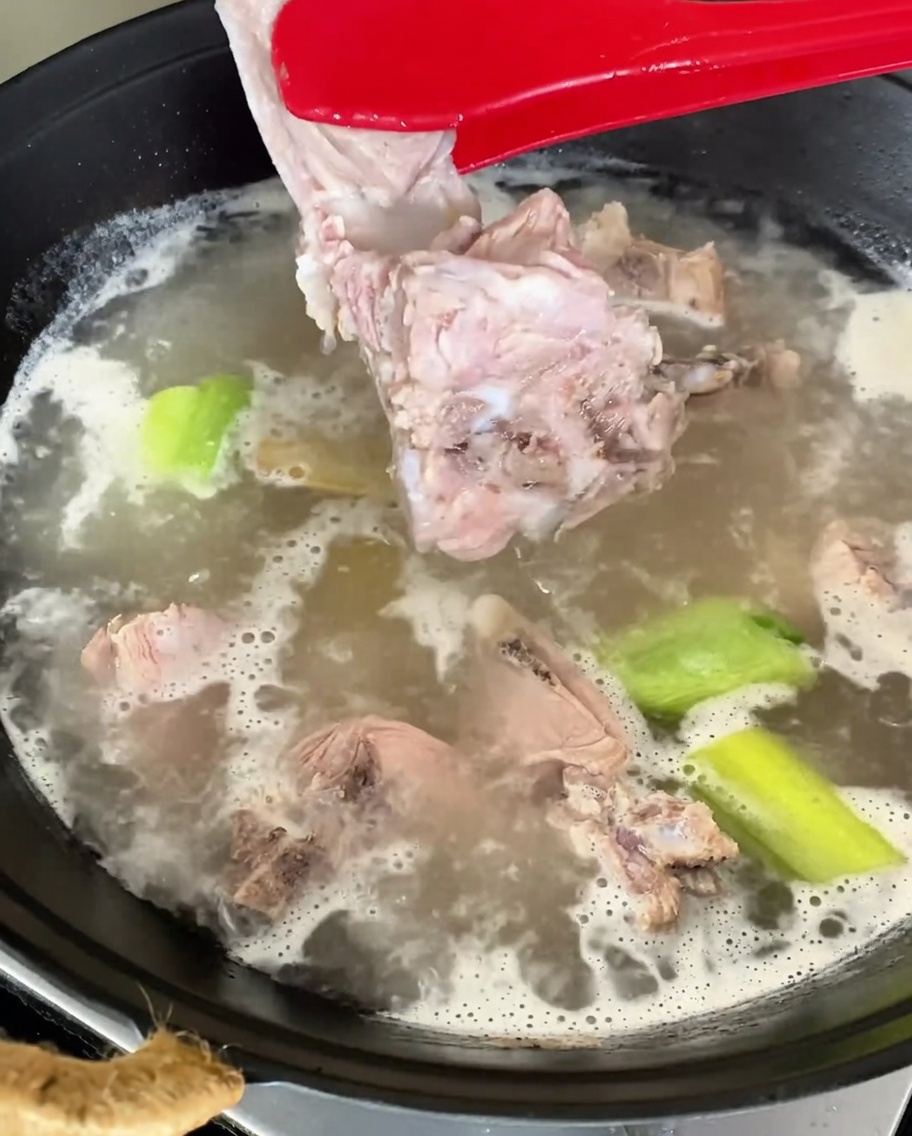 Morceaux déchine de porc blanchis retirés de leau bouillante à laide de pinces rouges.