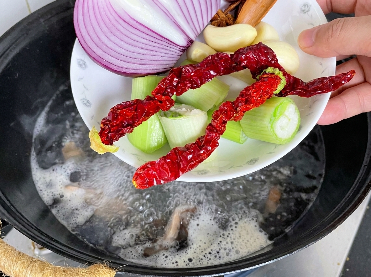 Échine de porc dans un wok avec des aromates et de leau bouillante versée par-dessus.