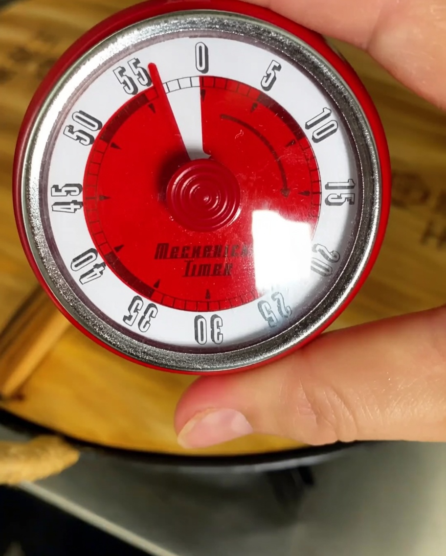 Minuteur de cuisine réglé sur une heure avec une casserole frémissante en arrière-plan.