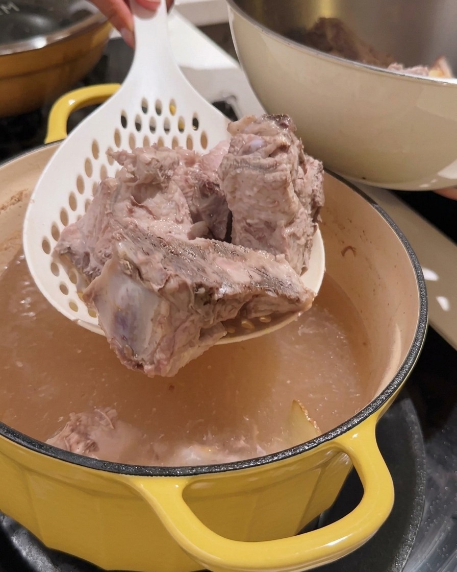 Une passoire retirant les morceaux de dos de porc blanchis dune marmite.