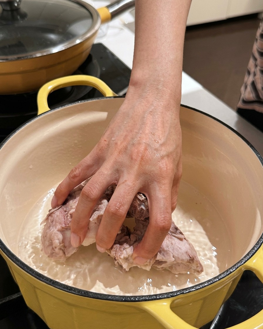 Une main plaçant des morceaux de dos de porc nettoyés dans une marmite propre.