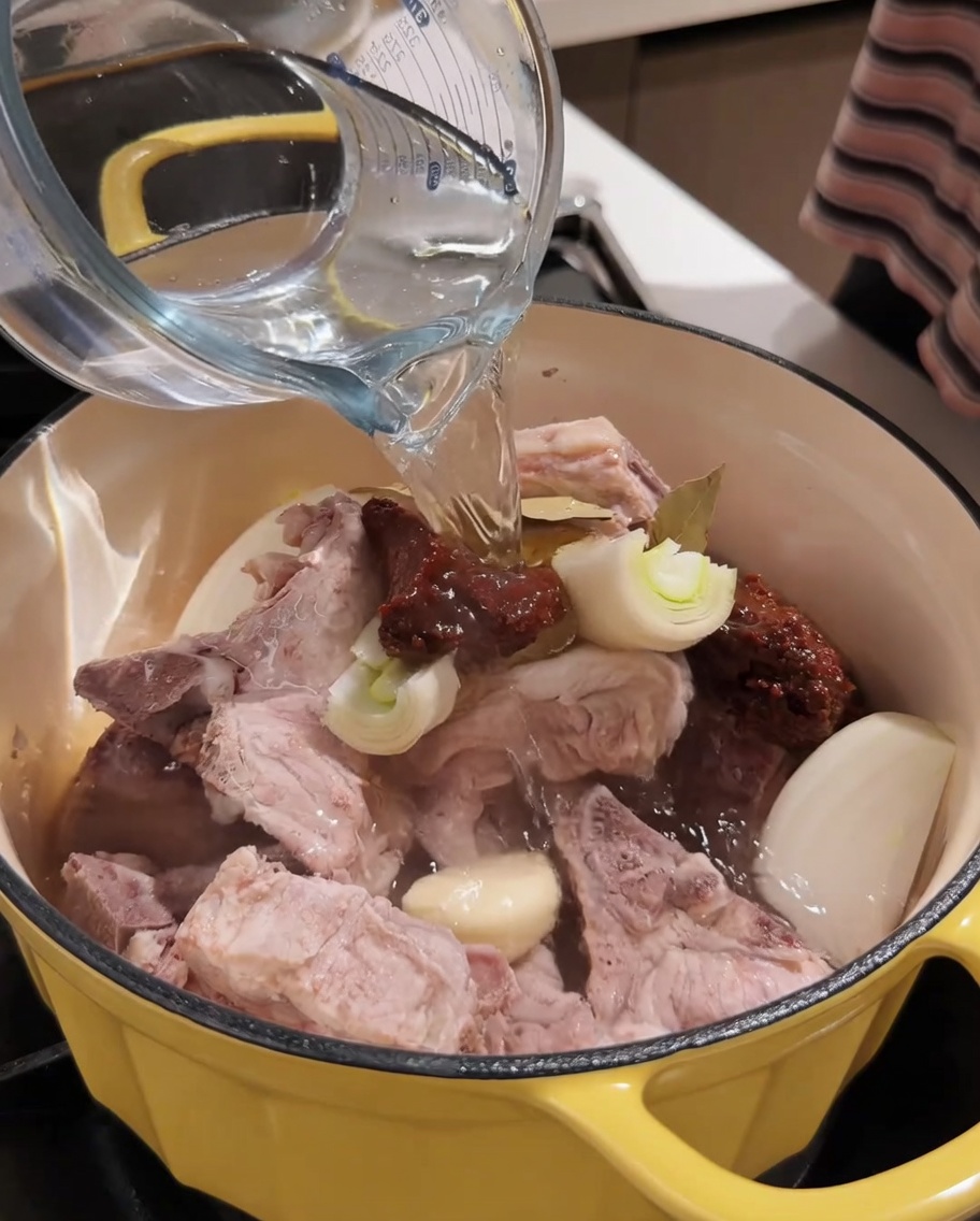 De leau bouillante versée dans la marmite avec le porc et les assaisonnements.