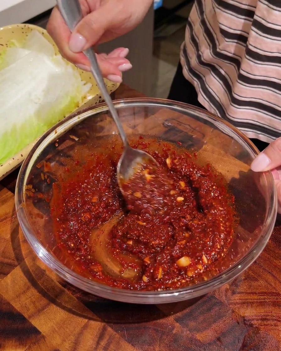 Des lanières de chou blanchi mélangées avec une sauce rouge dans un bol.