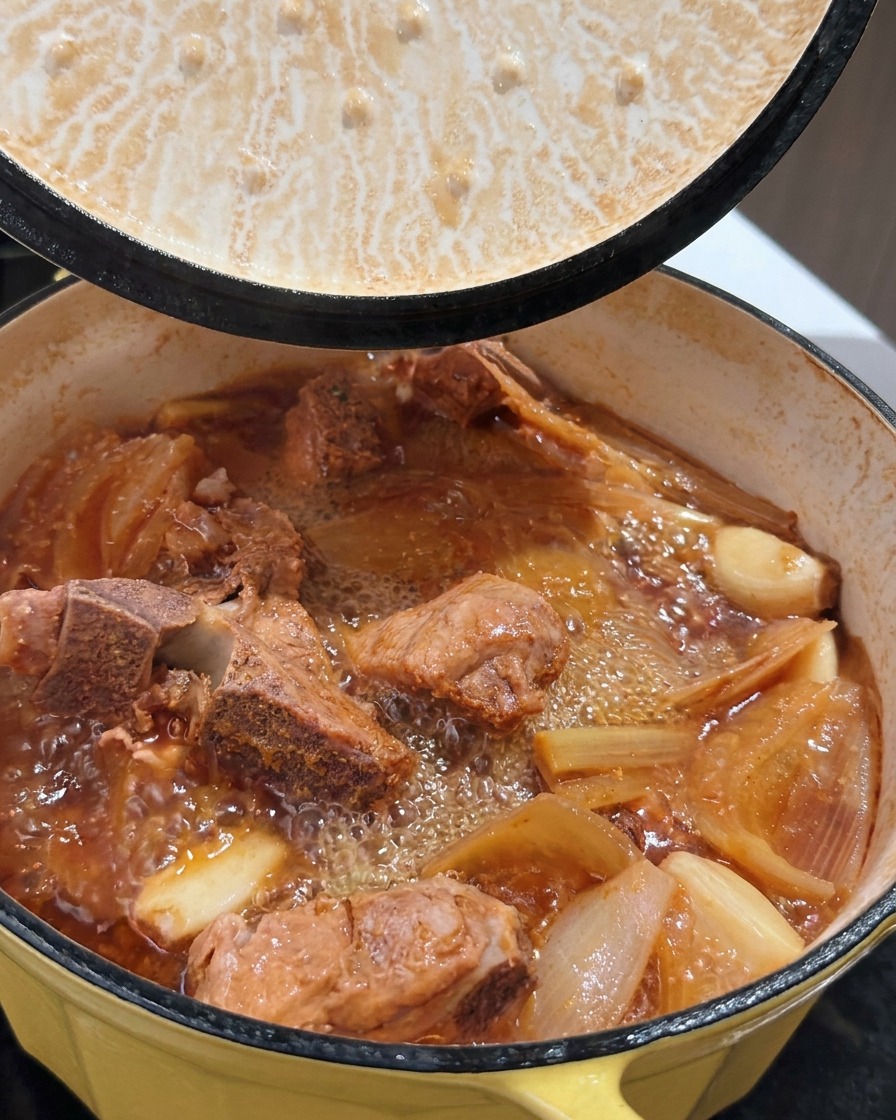 Une marmite de porc braisé bouillonnant avec un bouillon riche au moment où le couvercle est soulevé.