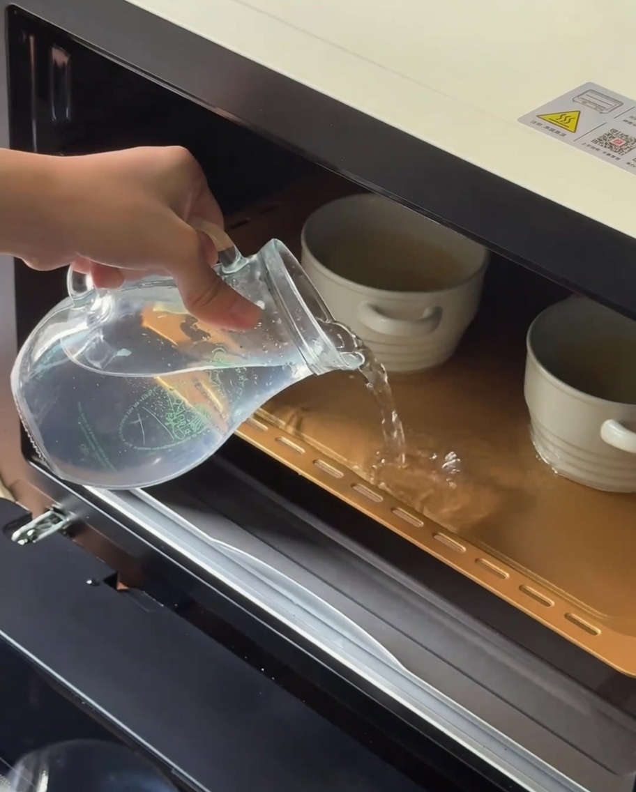 De leau tiède versée dune pichet en verre dans un plat de cuisson contenant des ramequins en céramique.