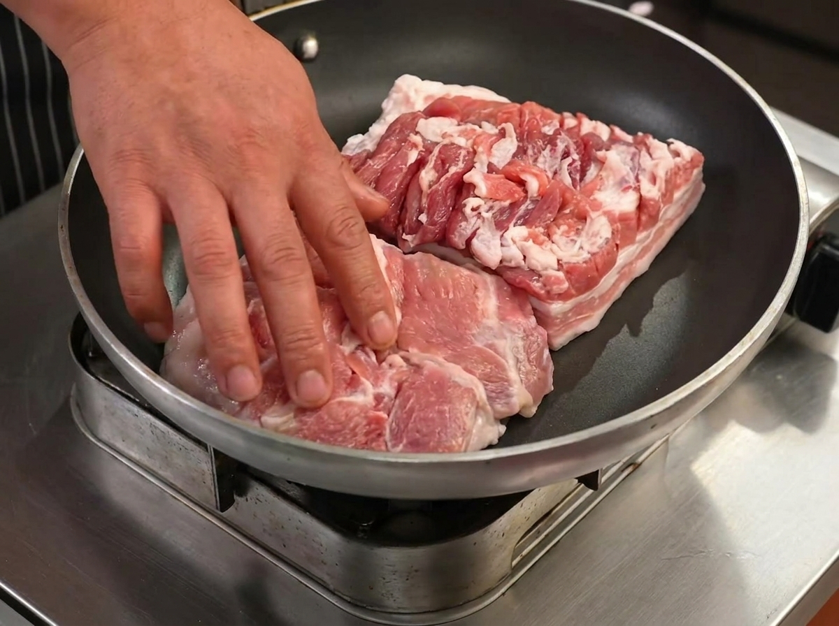 Tranches de poitrine de porc saisies dans une poêle sèche, commençant à dorer et à rendre leur gras.