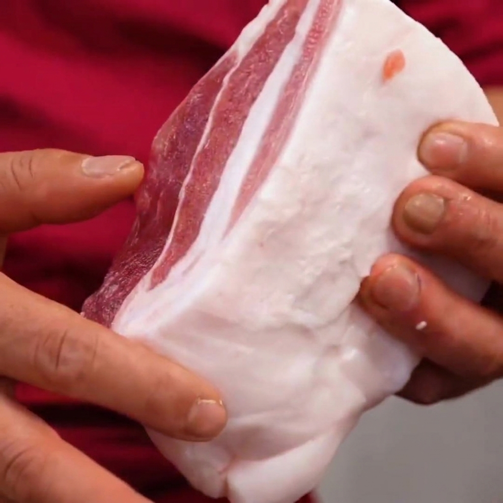 Poitrine de porc tenue dans les mains, montrant les coupes en quadrillage faites à un angle de 45 degrés.
