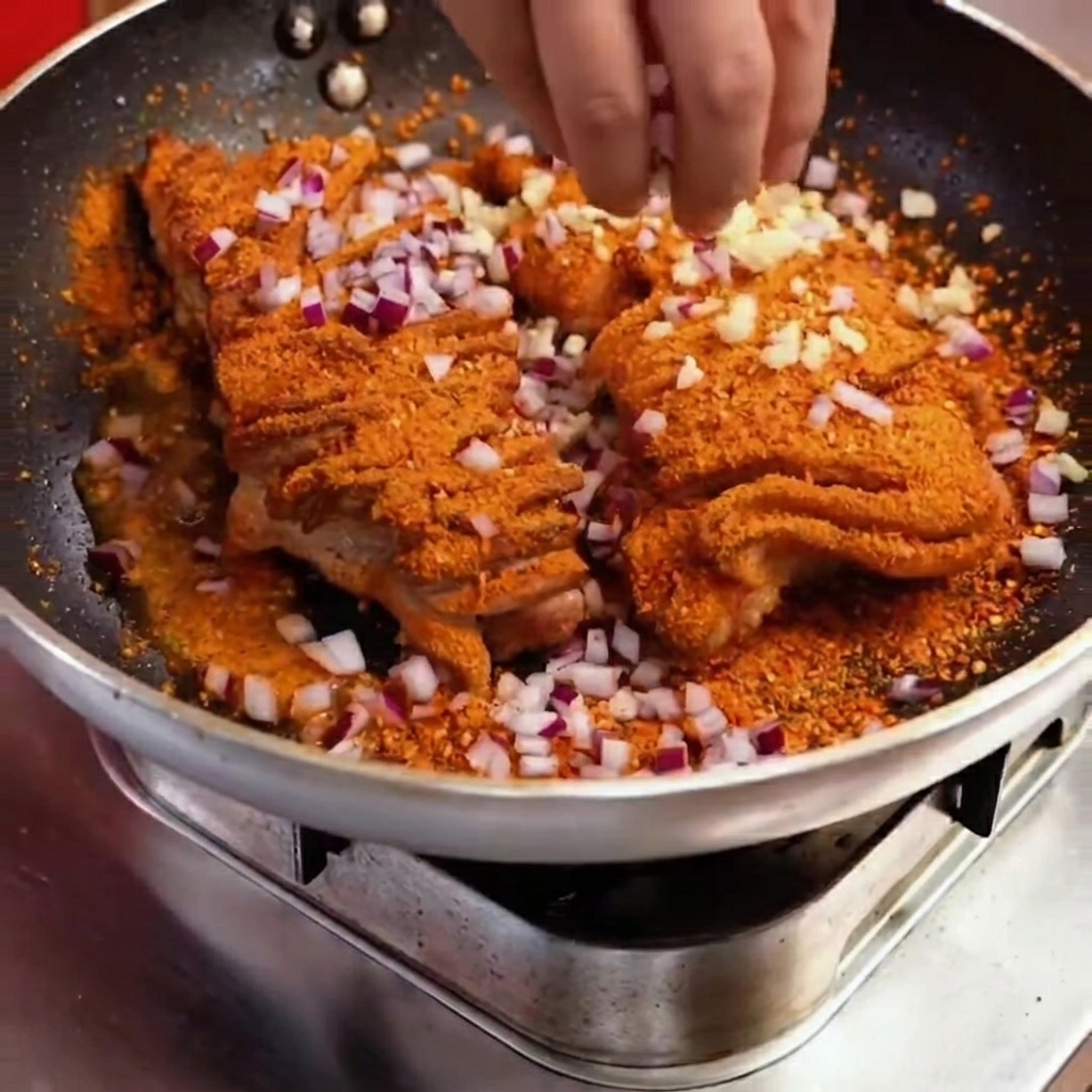 Gros plan de dés doignon rouge et de poivrons verts ajoutés sur le porc épicé dans la poêle.