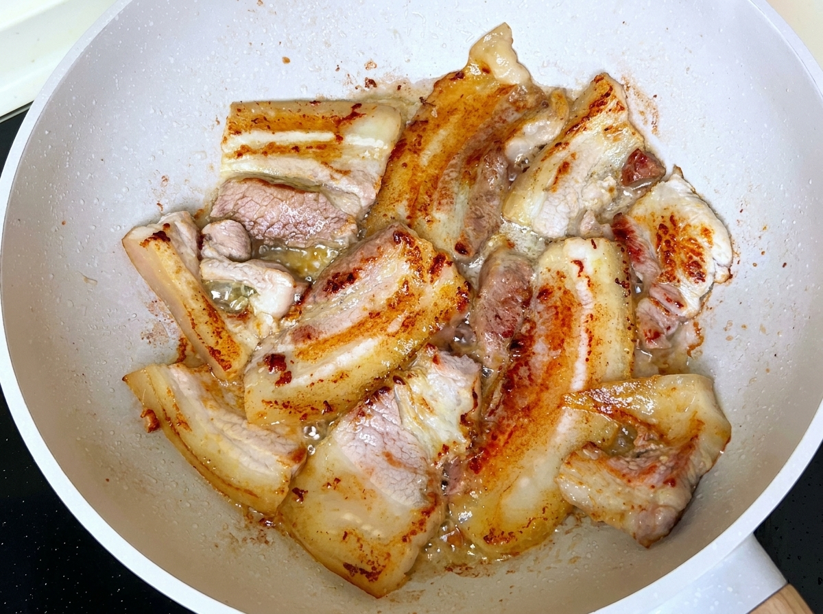 Tranches de poitrine de porc en train de frire et de brunir dans une poêle avec de la graisse fondue.