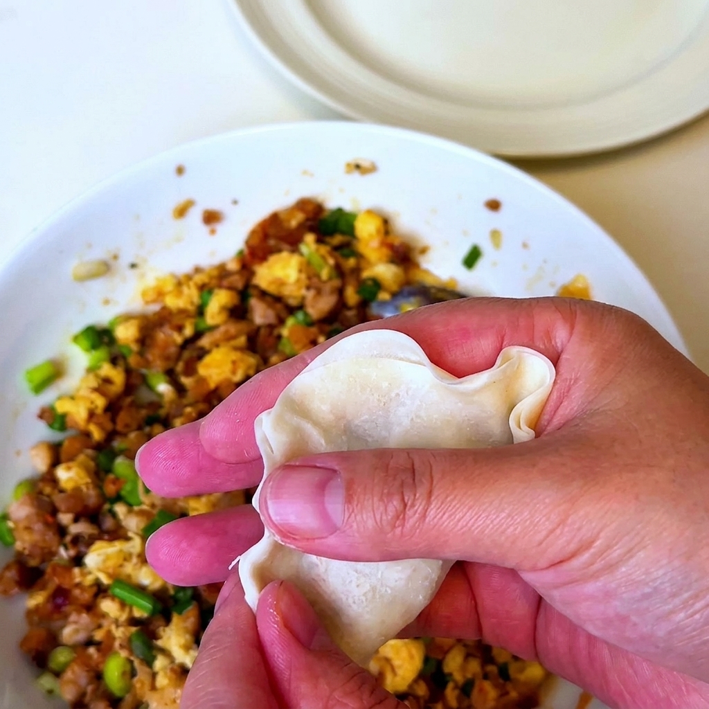 Une main tenant une feuille de ravioli garnie du mélange de porc barbecue et la refermant en la pliant.