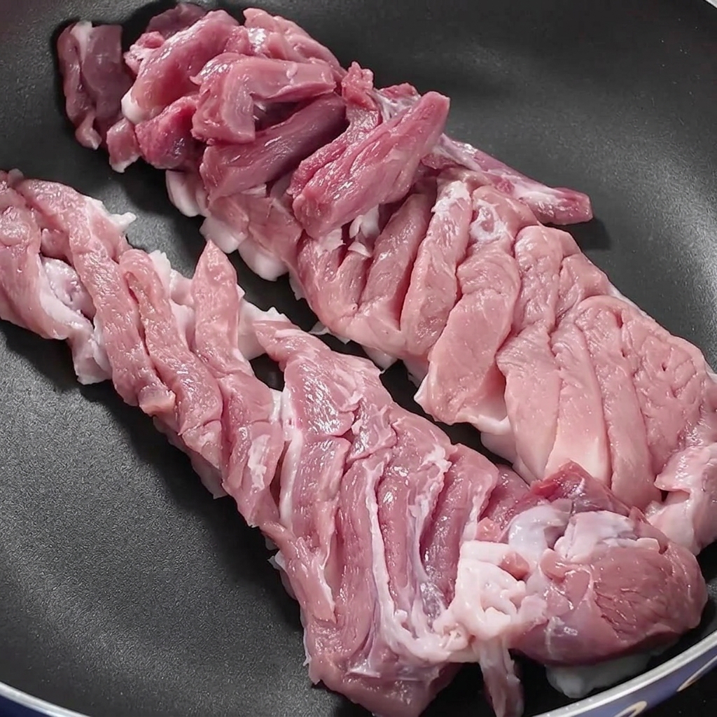 Tranches de poitrine de porc disposées soigneusement dans une poêle sombre sur un feu de cuisinière.