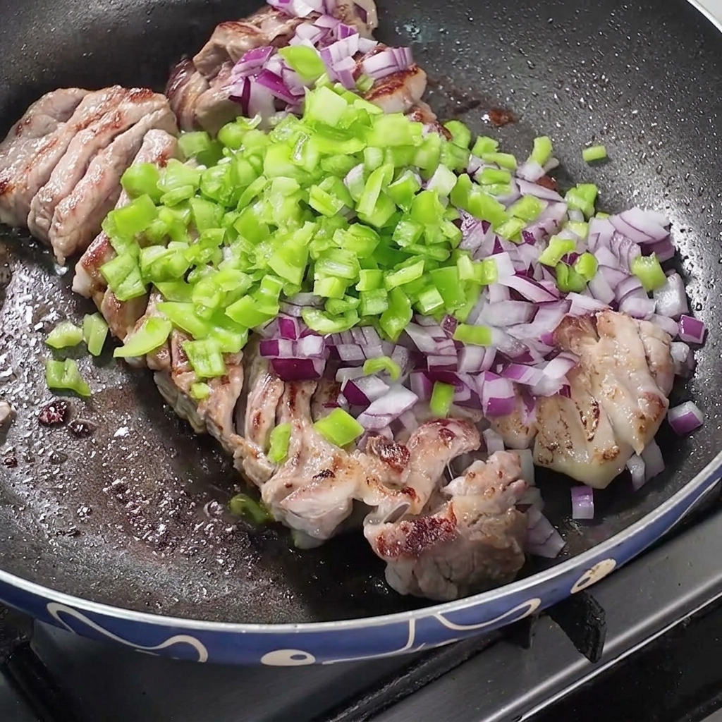 Une poêle contenant le porc en train de frire, agrémenté doignons hachés, de poivrons verts et dépices sèches.