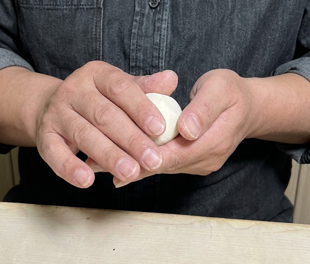 Des mains repliant et scellant délicatement un disque de pâte rempli de farce.