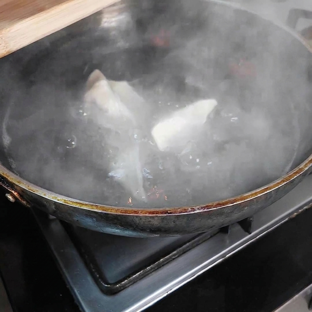 Plusieurs dumplings immergés dans une grande marmite deau bouillante, avec de la vapeur séchappant de la casserole.