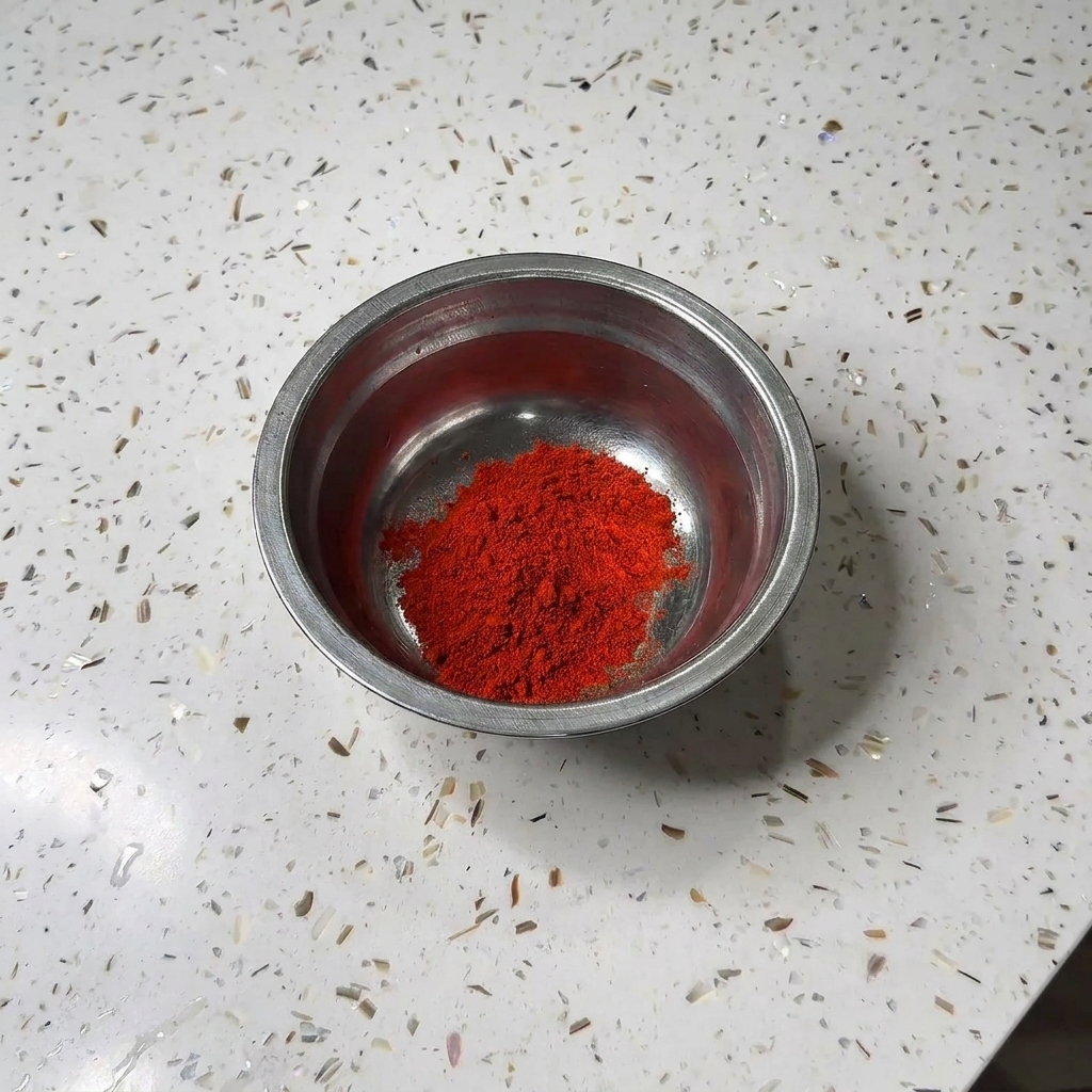 Un petit bol en métal contenant un monticule de poudre de piment rouge et de sucre blanc sur un comptoir en granit.