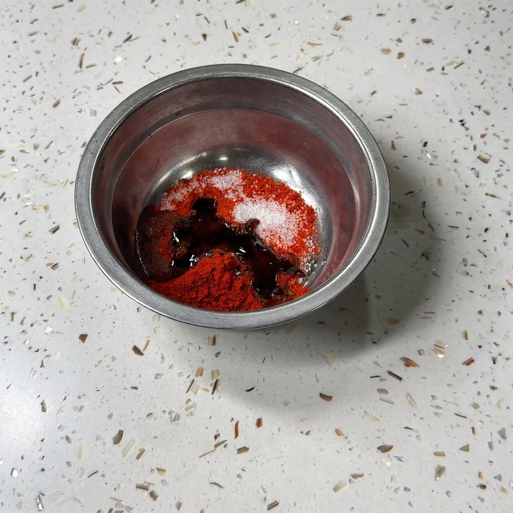 De la sauce soja noire et de la sauce huître versées dans le bol en métal avec la poudre de piment et le sucre.