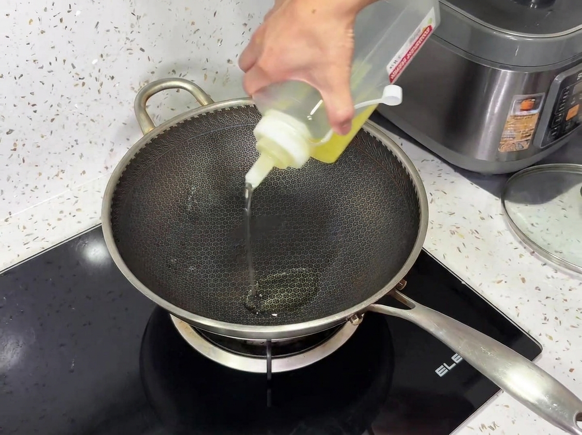 De lhuile de cuisson versée à partir dune bouteille compressible dans un wok en métal texturé sur une plaque à induction noire.