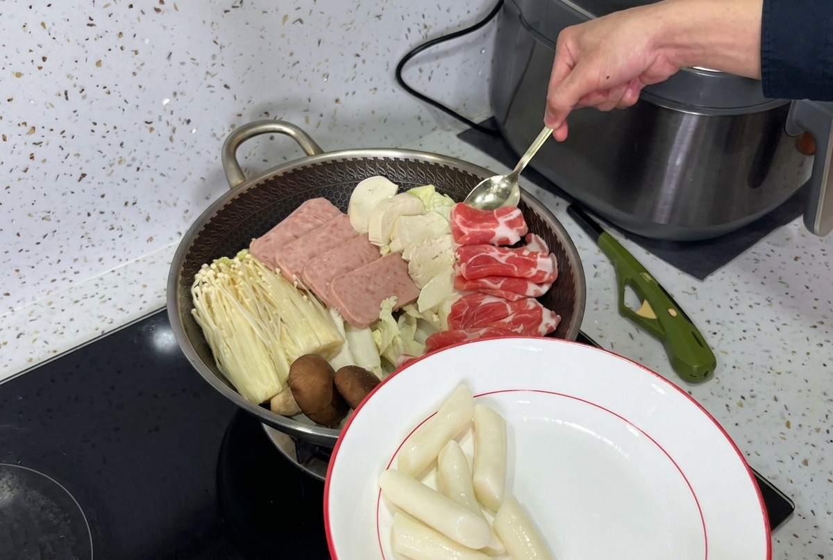 Une casserole magnifiquement agencée de ragoût de larmée coréenne, avec des couches de viande de luncheon, de champignons, de tofu et de kimchi frais prêts pour le bouillon.