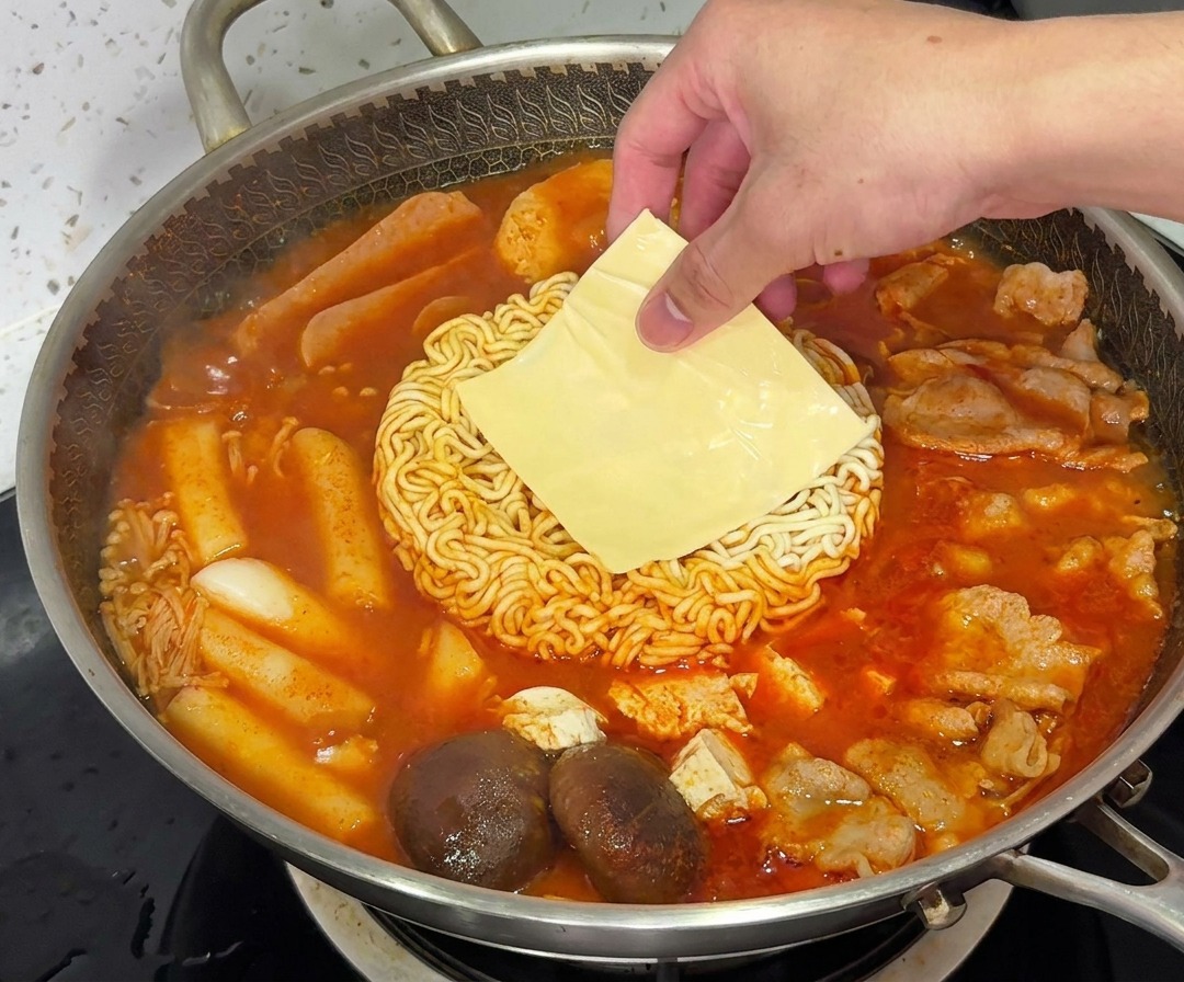 Une tranche de fromage jaune fondant sur les nouilles ramen dans une casserole fumante de Budae Jjigae.