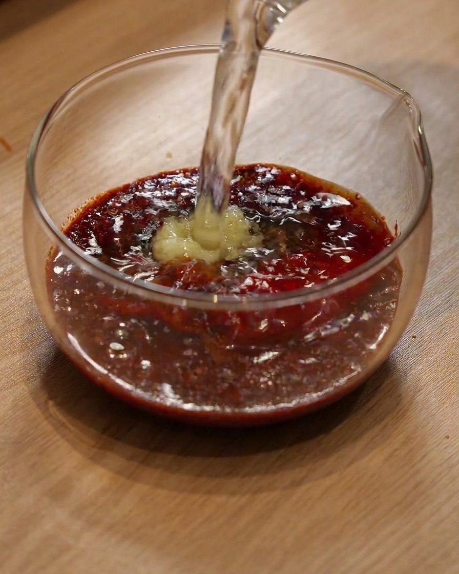 De leau versée dans un bol en verre contenant du piment en poudre et des assaisonnements.