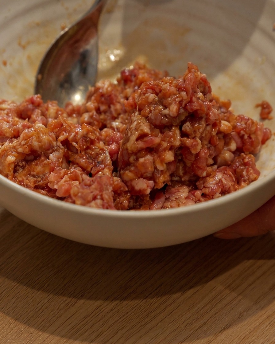 Porc haché en cours de marinage dans un bol blanc avec une cuillère.