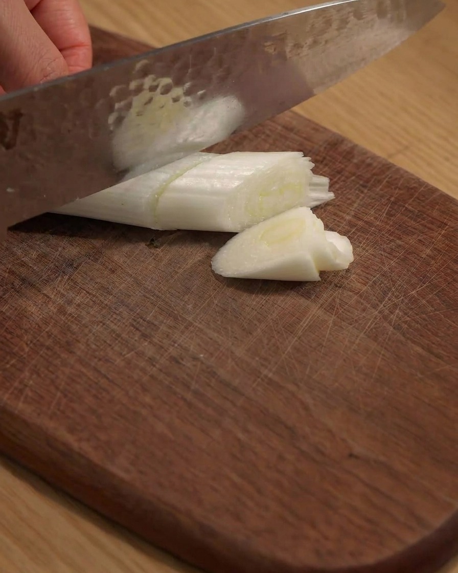 Un couteau coupant un grand oignon vert en morceaux sur une planche en bois.