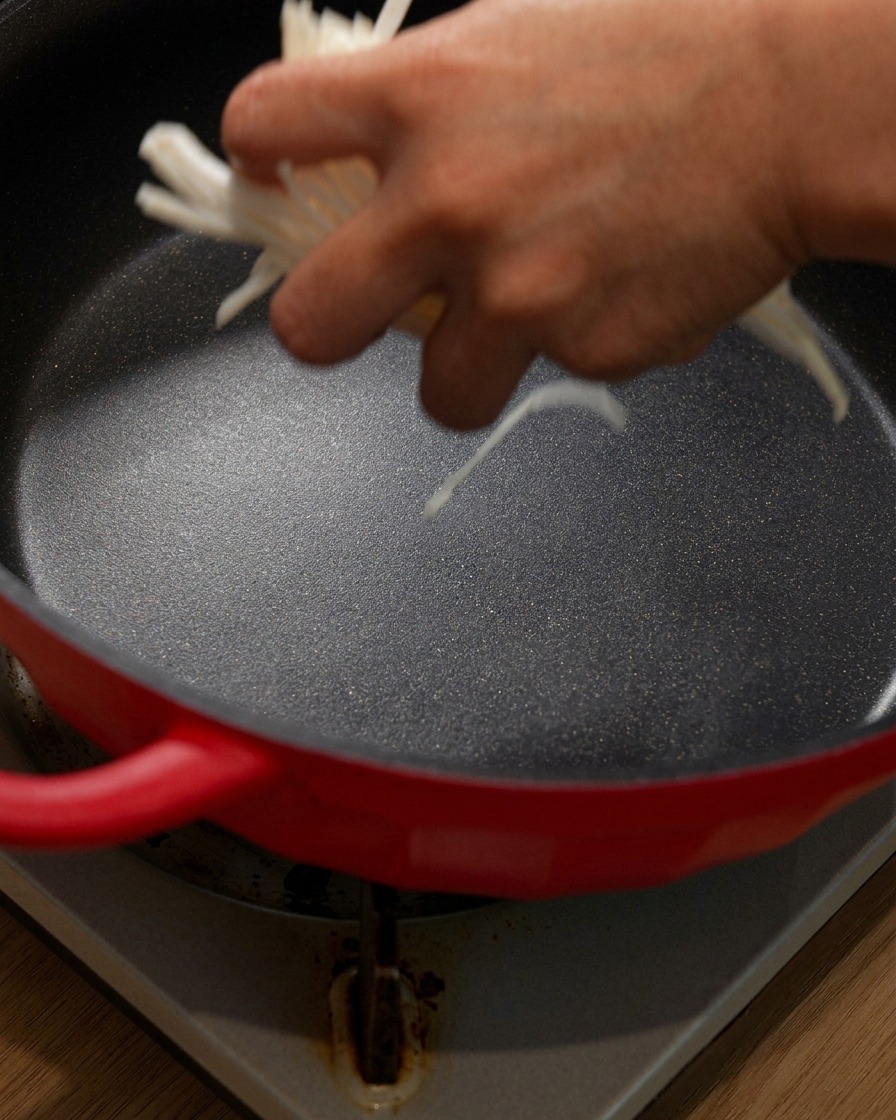 Oignons émincés ajoutés au fond dune cocotte rouge.