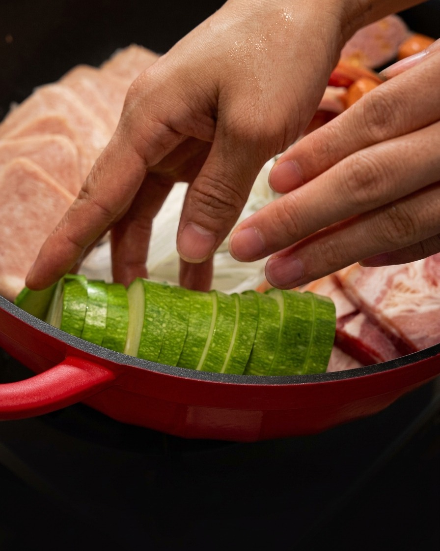 Tranches de courgette disposées soigneusement dans la cocotte rouge à côté de la viande.