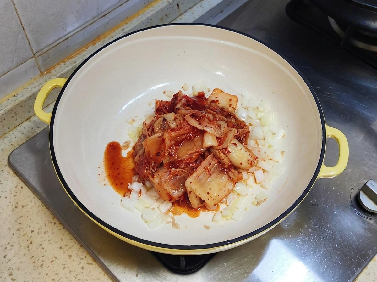 Une portion de kimchi rouge fermenté reposant sur des oignons sautés dans une poêle blanche.