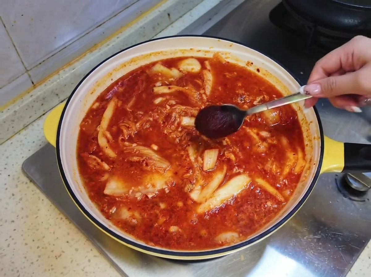Une cuillerée de sauce piquante coréenne abaissée dans le bouillon de soupe rouge à lintérieur de la poêle.