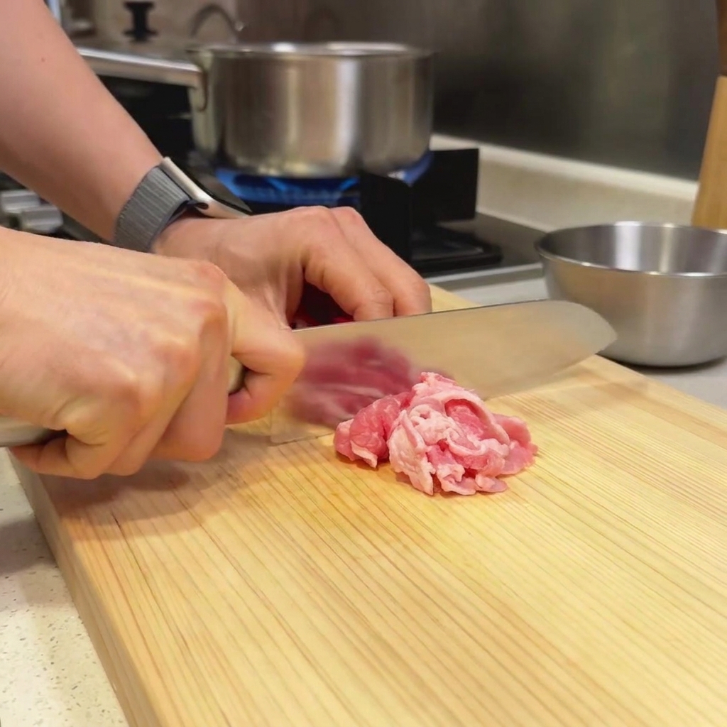 Fines tranches de bœuf disposées sur une planchette en bois prêtes à être découpées avec un couteau de chef.