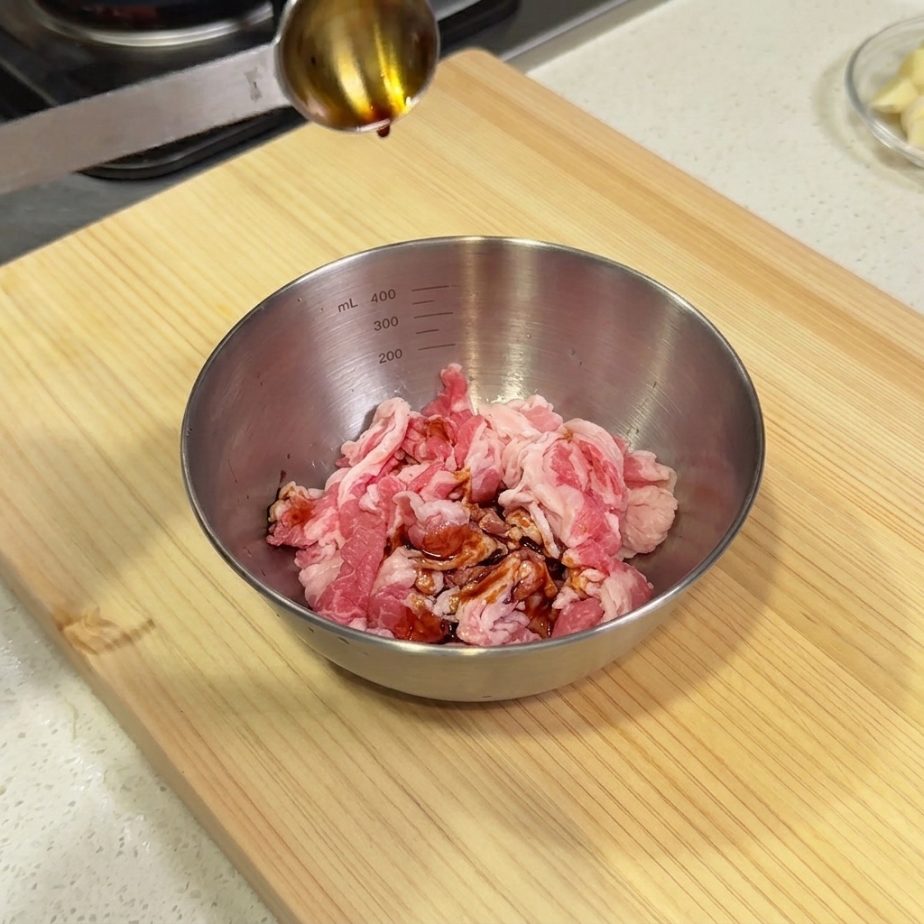 Versement de sauce soja à laide dune cuillère de mesure dans un bol en acier contenant des morceaux de bœuf cru.
