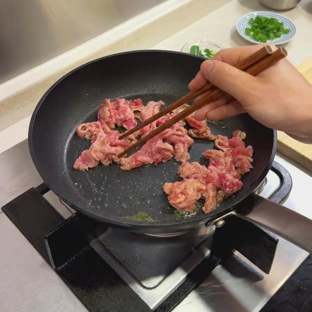 Tranches de bœuf marinées en cours de cuisson dans une poêle noire à laide de baguettes en bois.