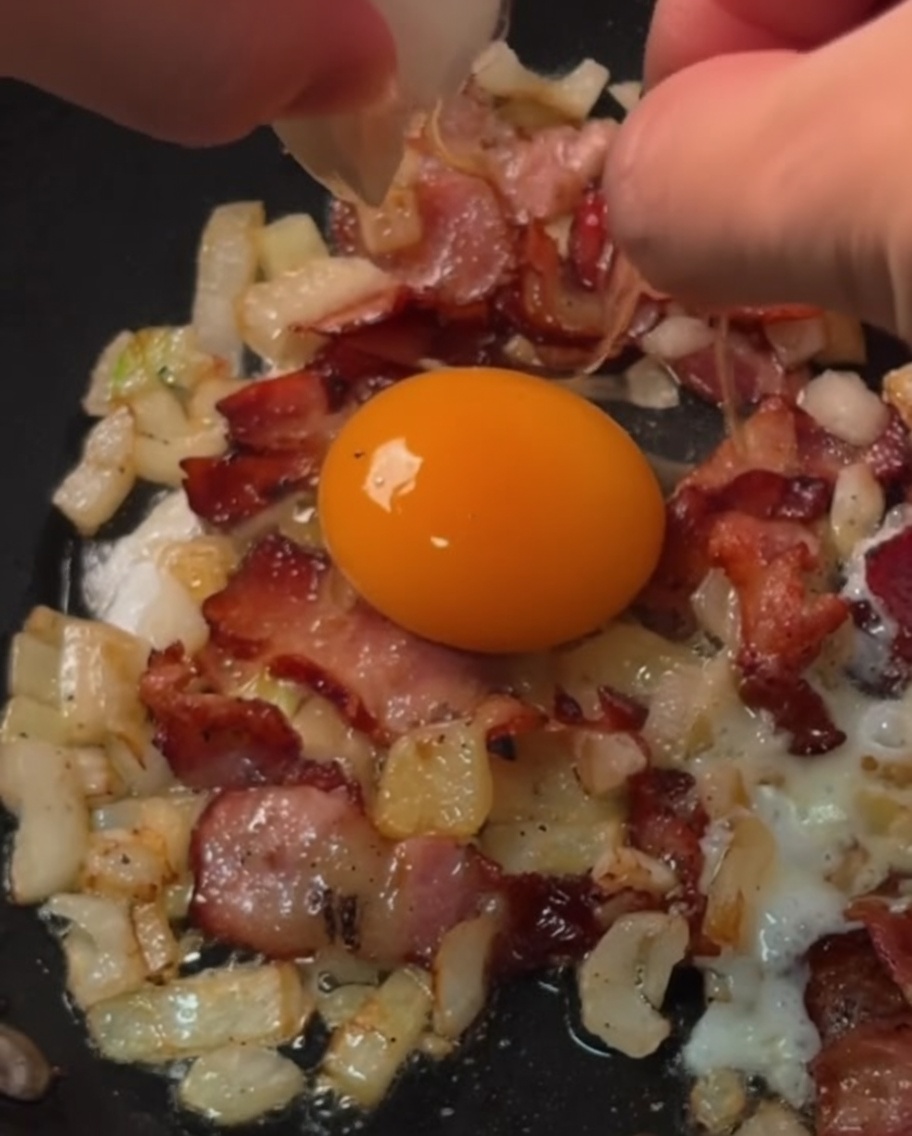 Des œufs frais cassés dans des anneaux individuels de bacon et doignon en train de cuire dans une poêle.
