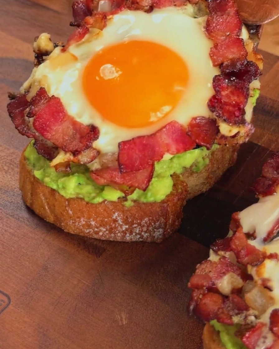 Un anneau de bacon et dœuf cuit placé sur une tartine à lavocat avec une spatule en bois.